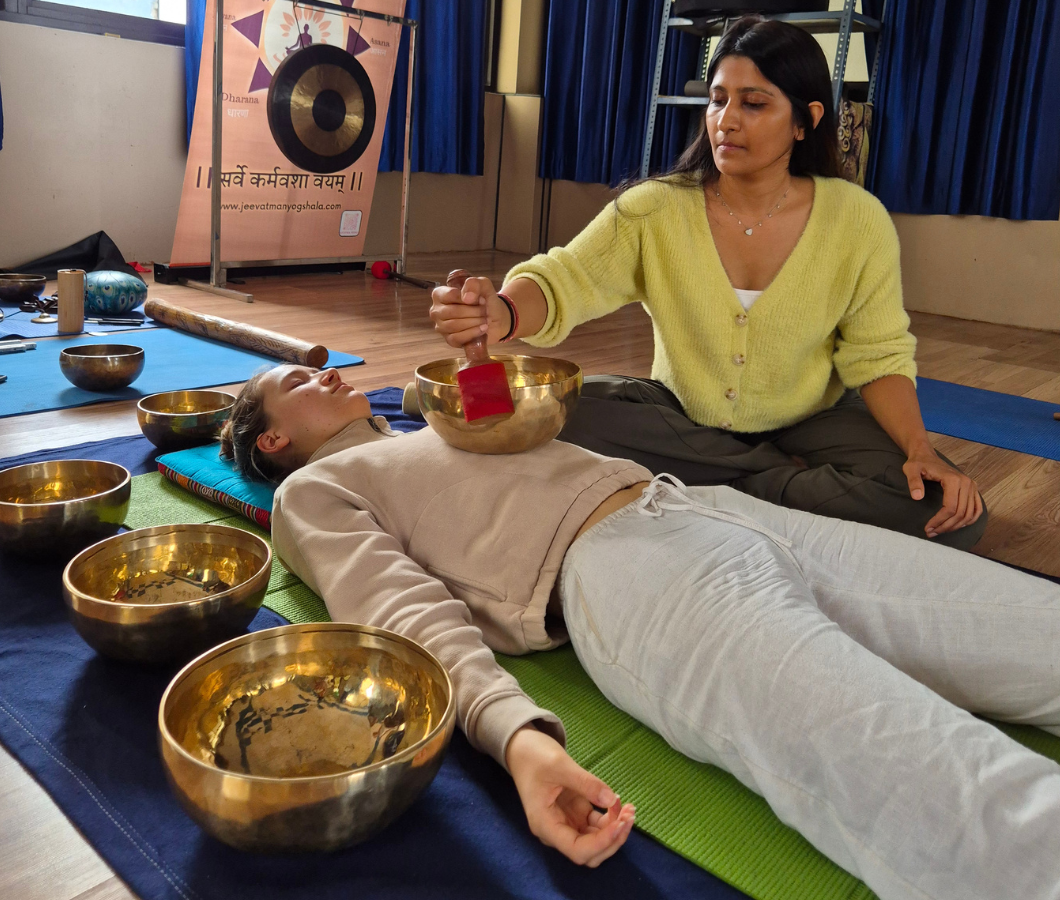 Woman performing Tibetan singing bowl sound healing therapy session on student at yoga school in Rishikesh